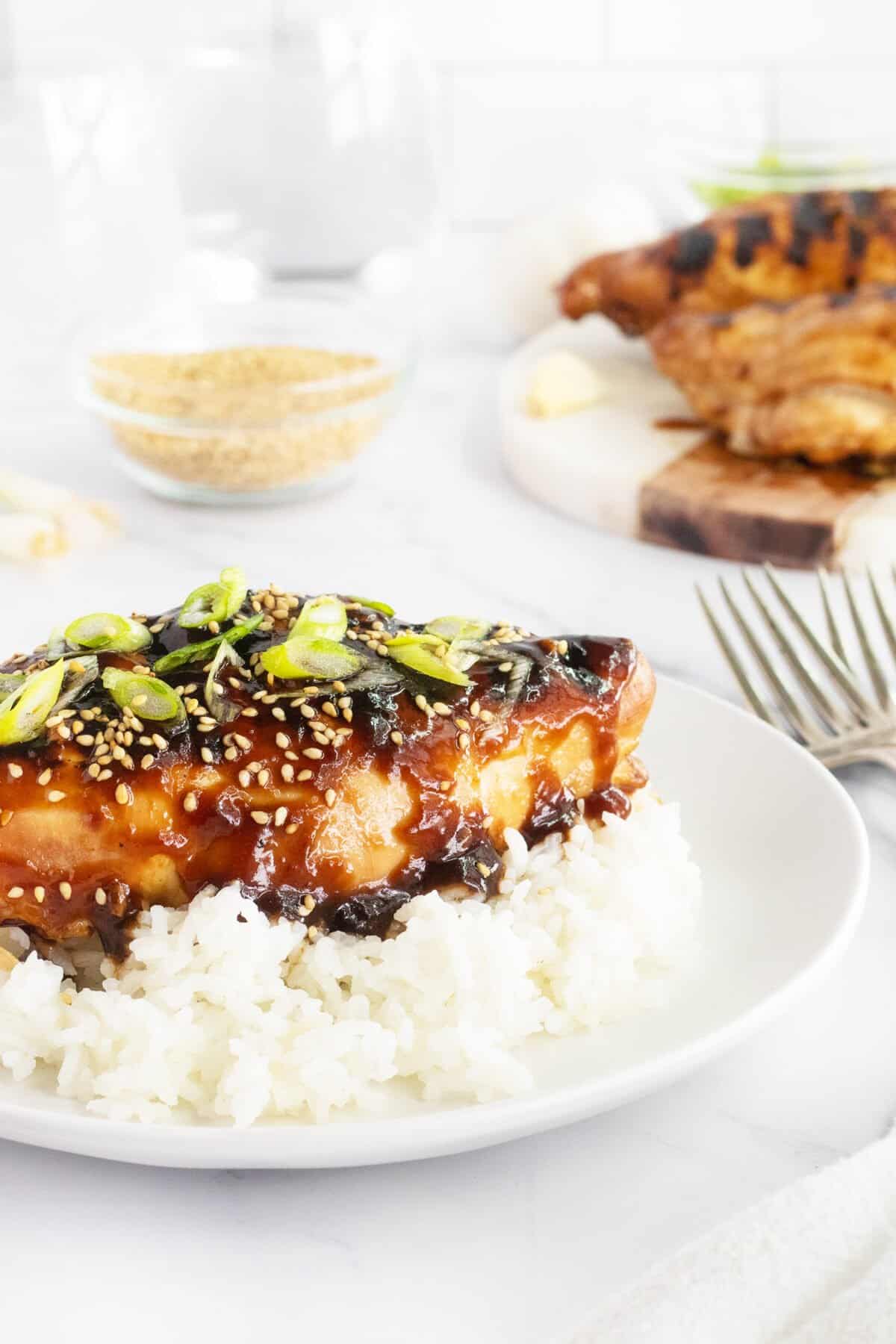 Grilled teriyaki chicken on a white plate with green onions on top