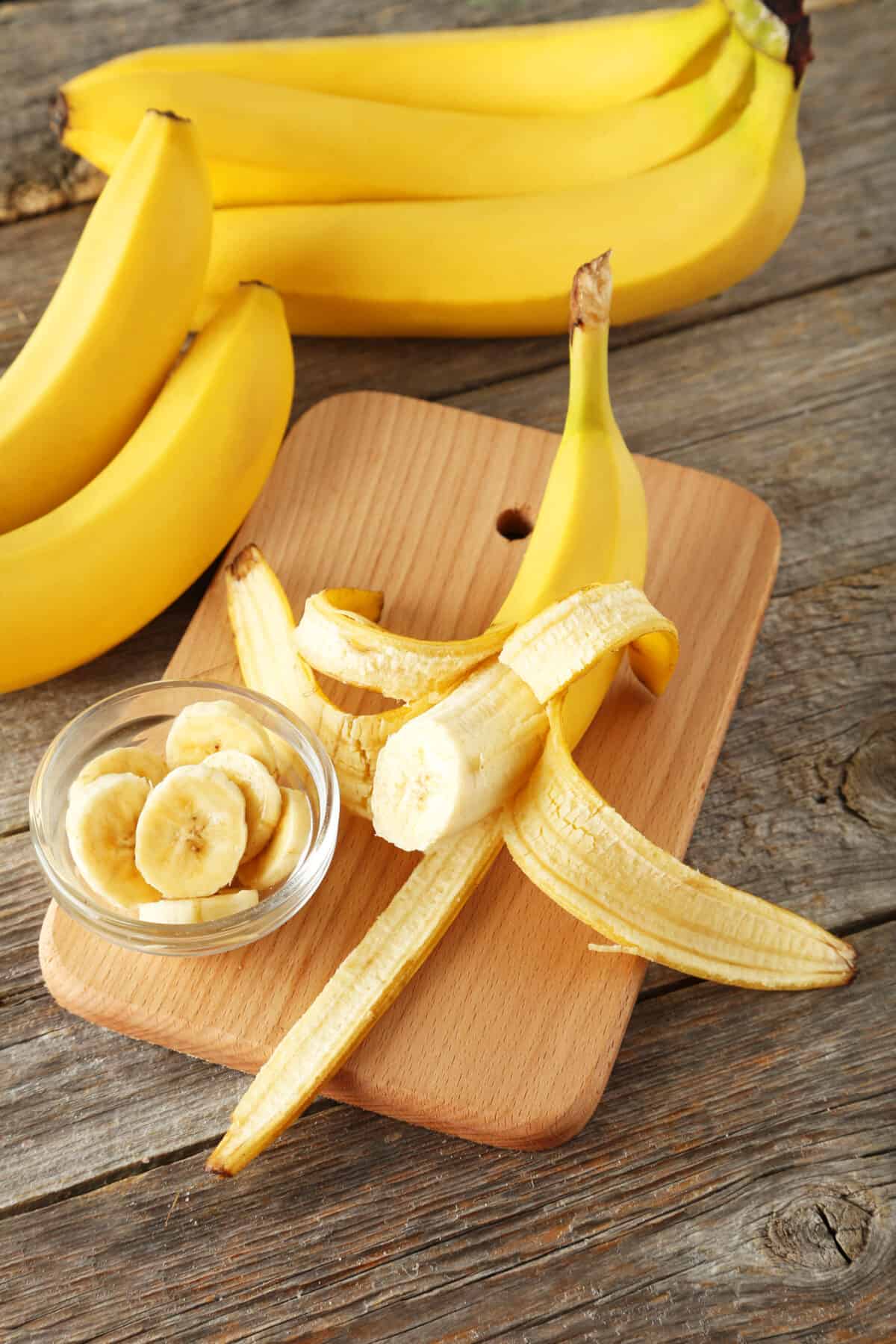 banana bunches and an open banana on a wooden cutting board