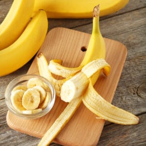 banana bunches and an open banana on a wooden cutting board