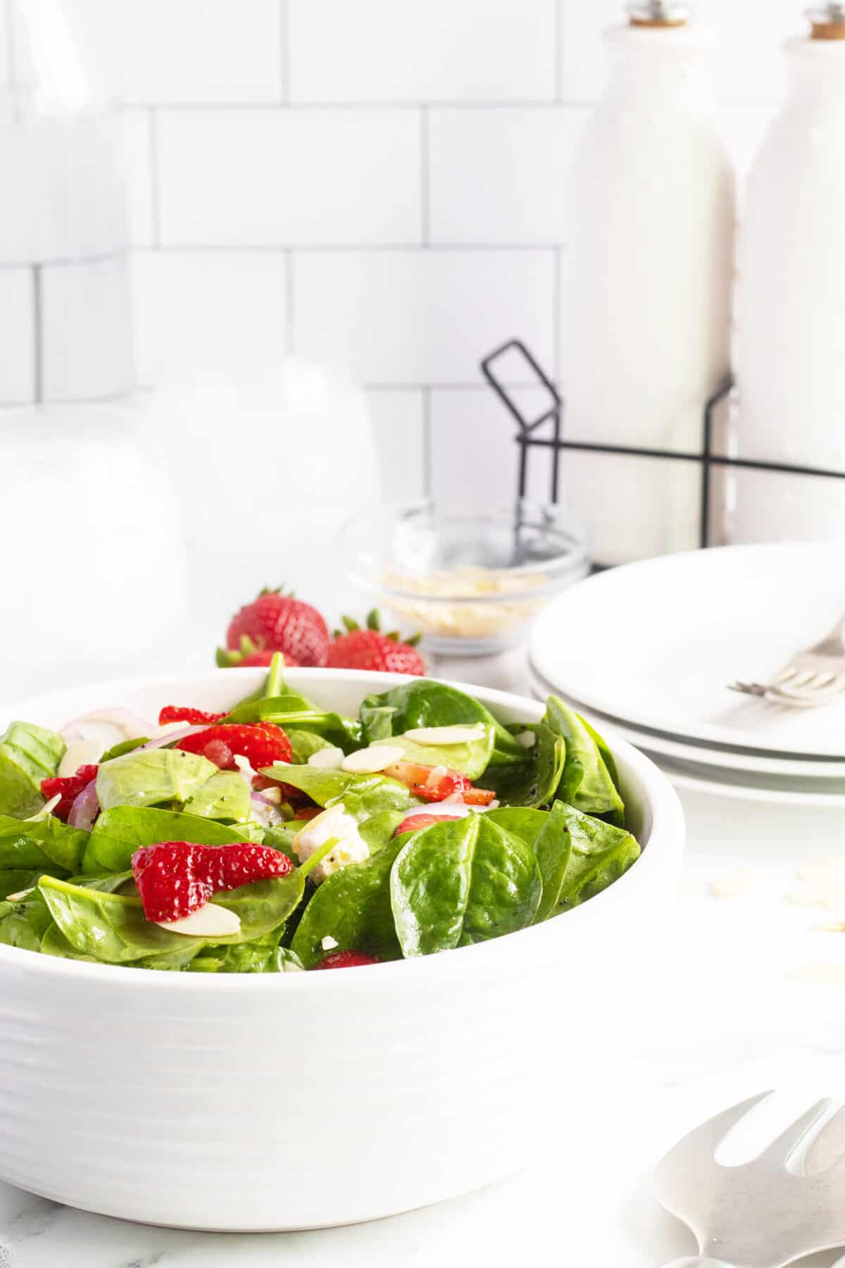Strawberry spinach salad i a white bowl and plates behind
