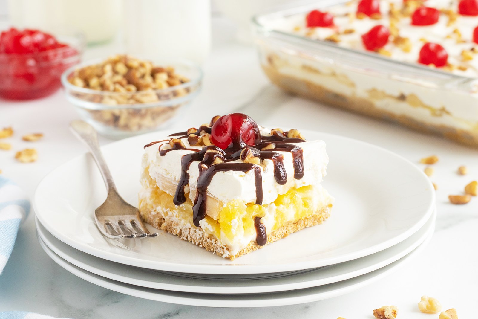 Banana split cake with whipped cream, cherries, and drizzle on top.