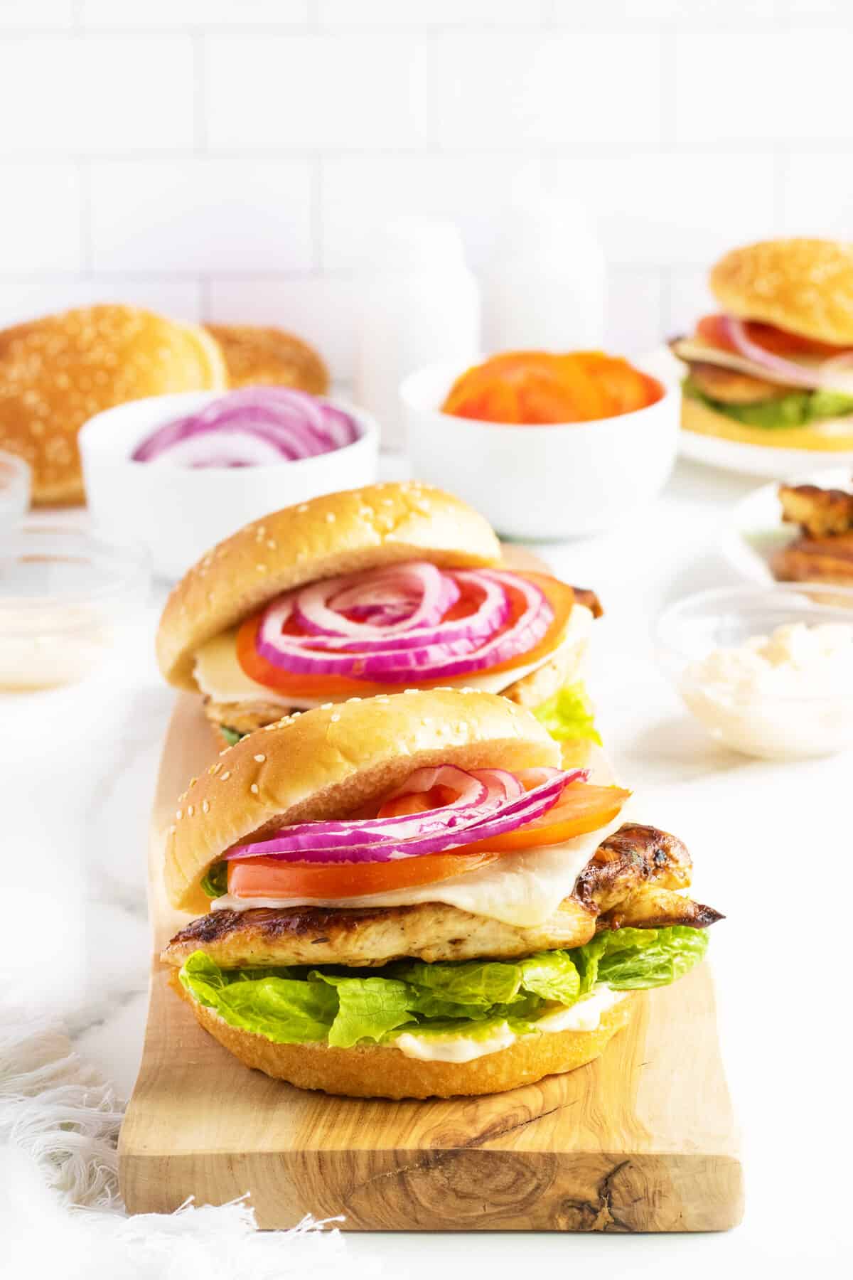 grilled chicken sandwiches on a wood cutting board with toppings