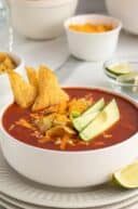 Chicken tortilla soup in a white bowl with tortilla chips and avocado slices