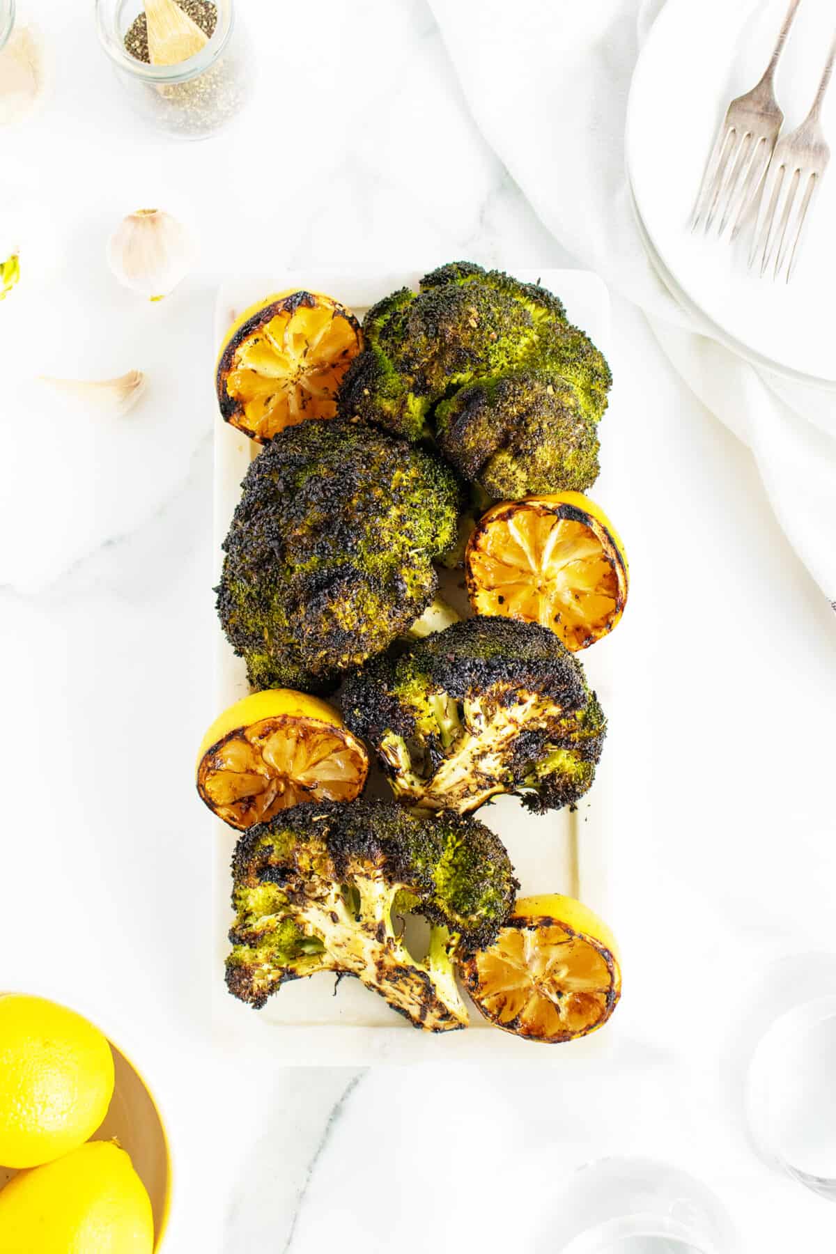 grilled broccoli on a white cutting board with lemons