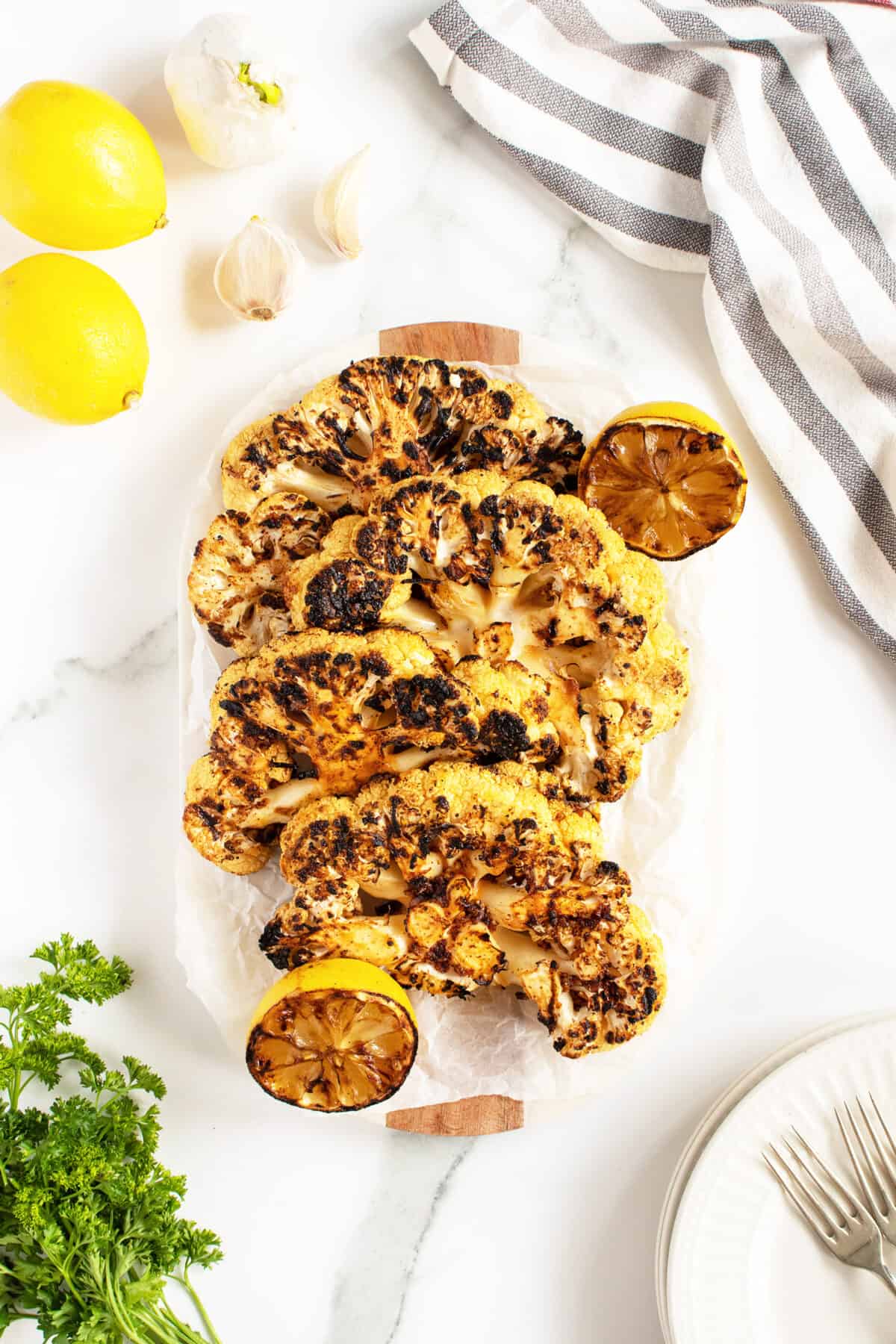 grilled cauliflower steaks lined up on a long white platter with grilled lemon