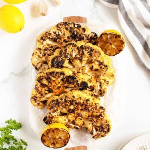 grilled cauliflower steaks lined up on a long white platter with grilled lemon