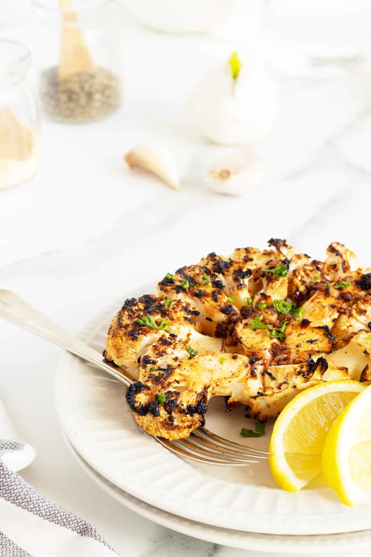 grilled cauliflower steaks on a white plate with a fork and lemon slices