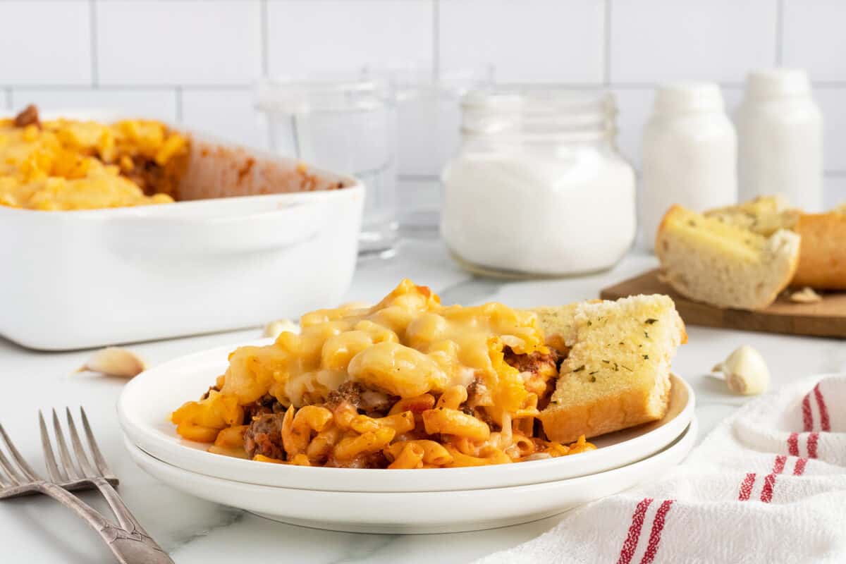 mac and cheese lasagna on a white plate with garlic bread