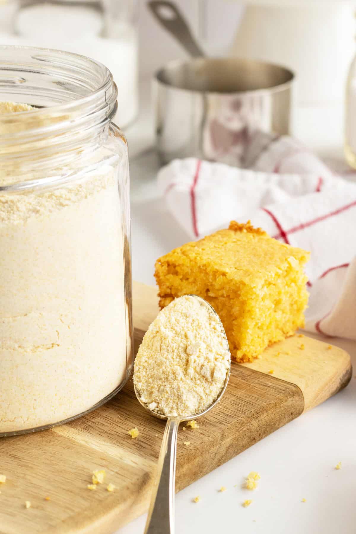 homemade cornbread mix in a glass container on a cutting board with spoon