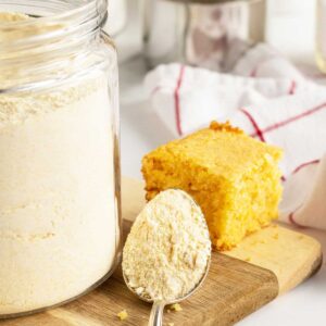 homemade cornbread mix in a glass container on a cutting board with spoon