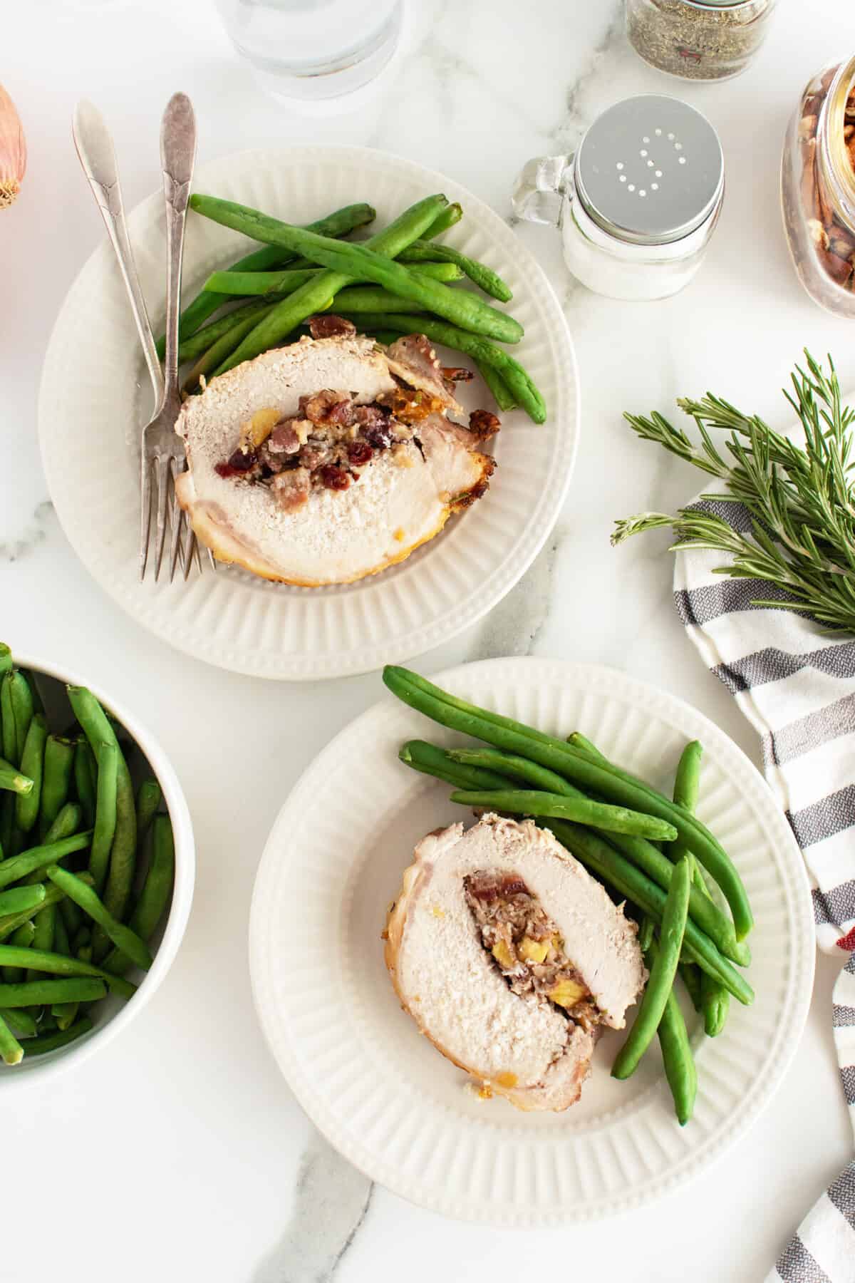 stuffed pork loin on two plates with green beans