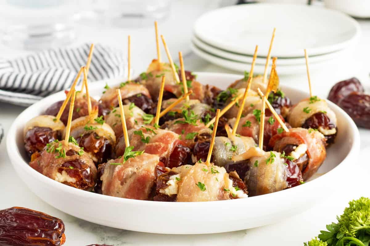 bacon wrapped dates on a white plate with toothpicks in them