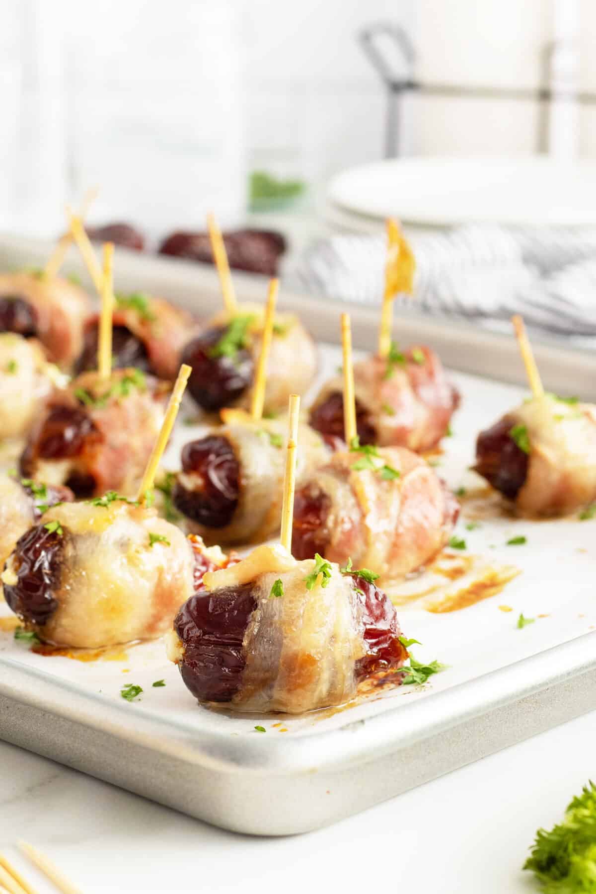 bacon wrapped dates with toothpicks on a baking tray