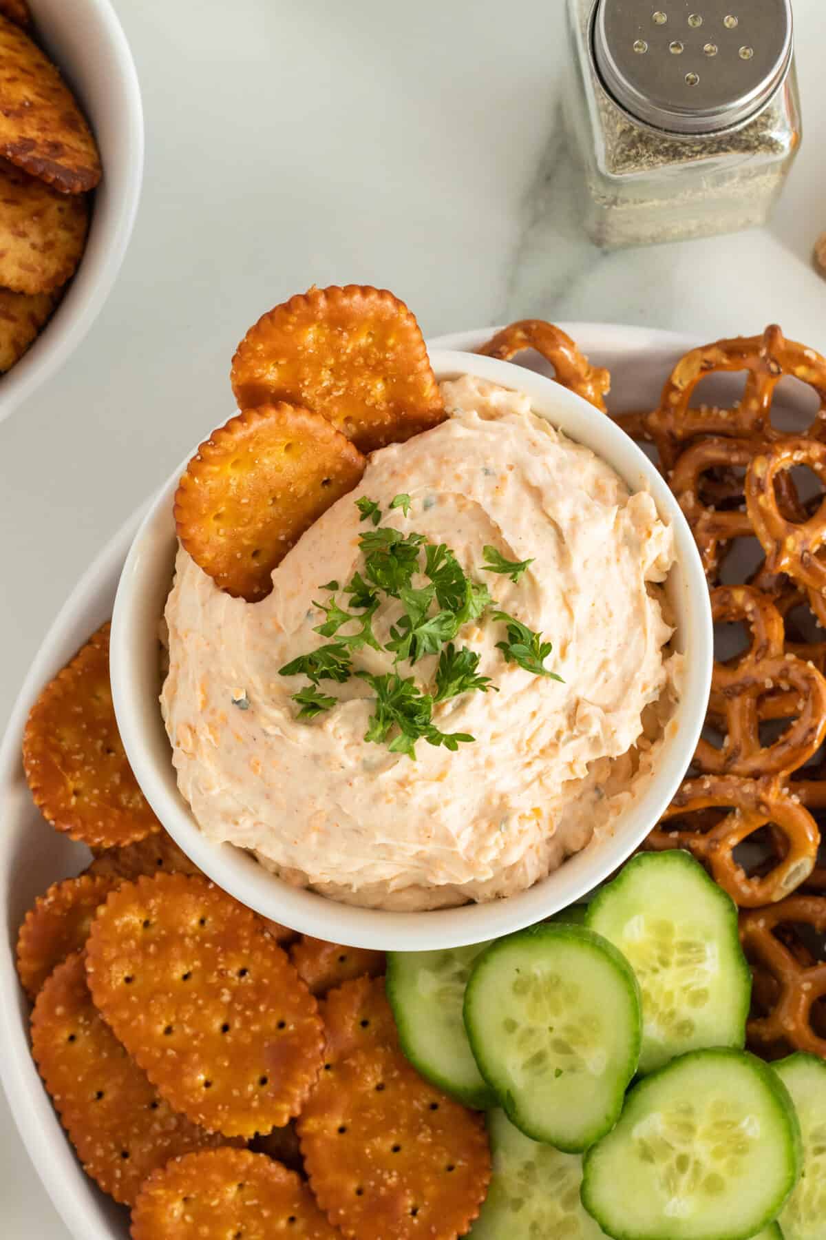 beer cheese dip in a bowl surrounded by crackers, pretzles and cucumber slices