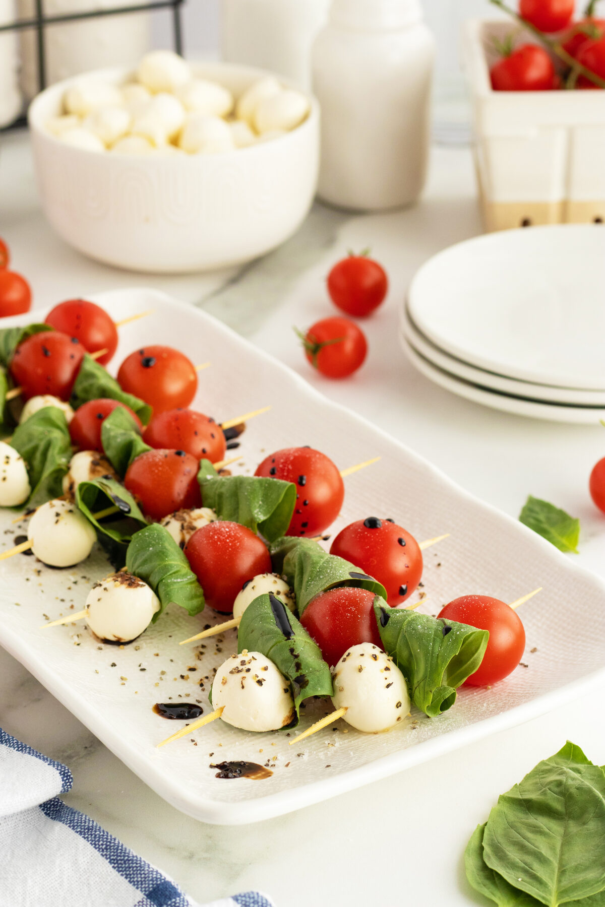 caprese skewers  lined up on a white platter with balsamic drizzle on them