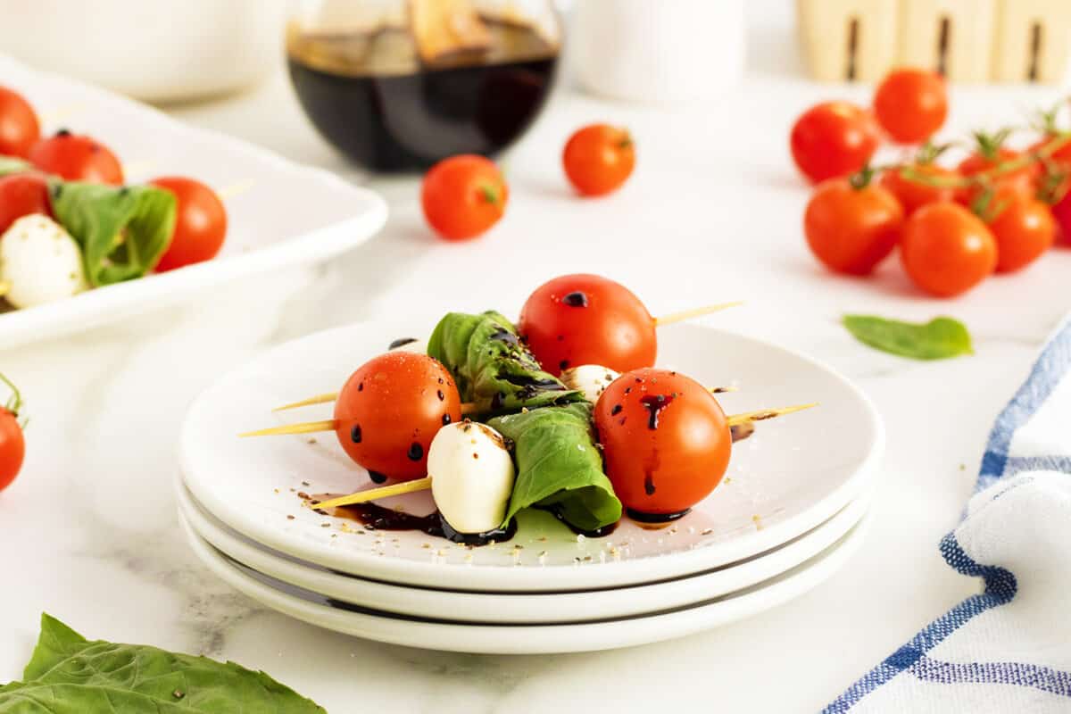 caprese skewers on a stack of white plates