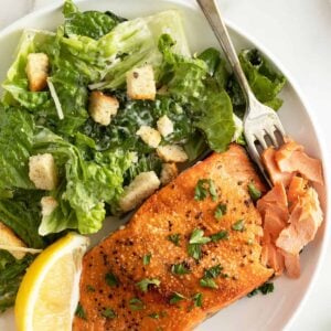 Air fryer salmon on a white plate with a caesar salad