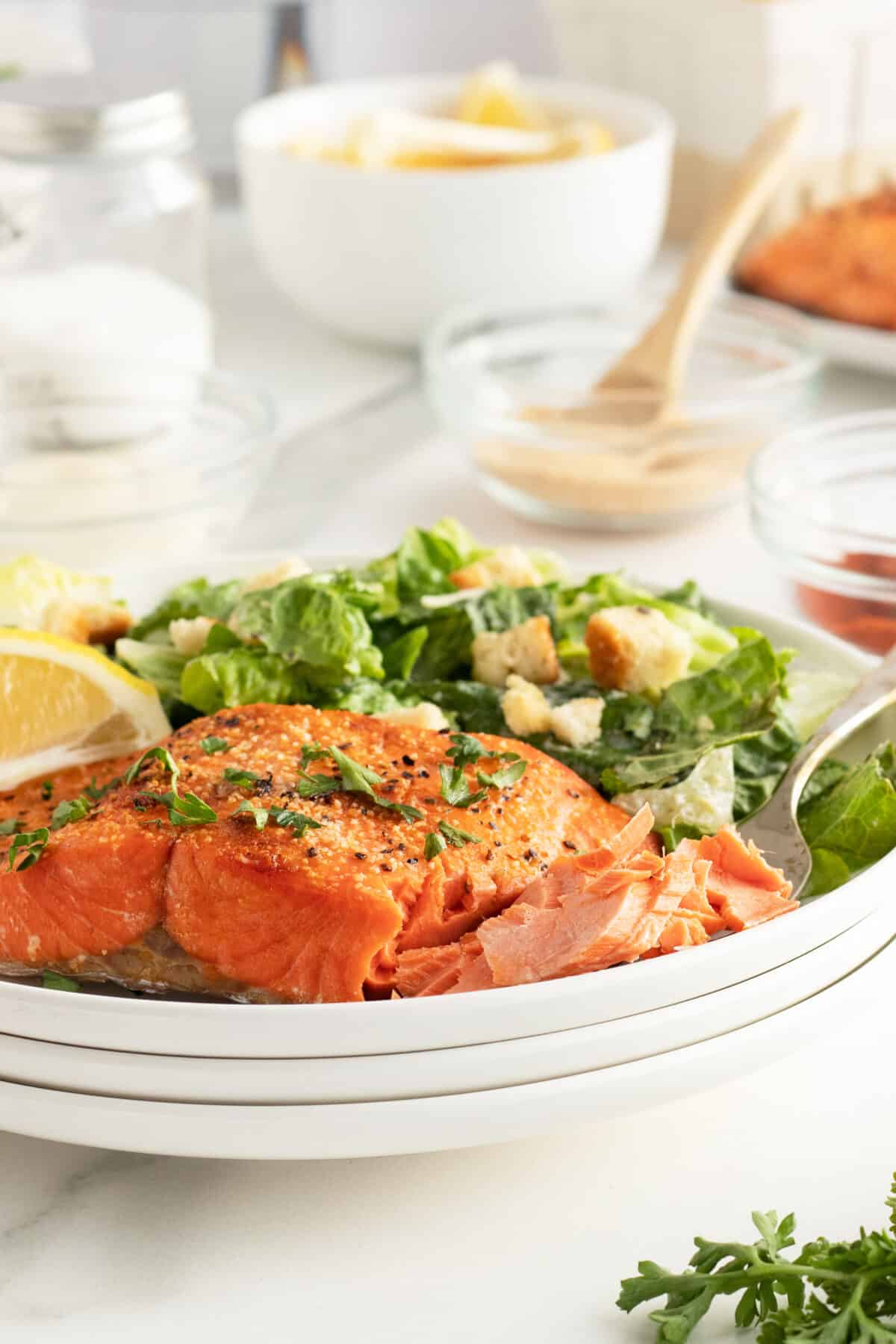Air fryer salmon on a plate with a caesar salad and slices of lemon