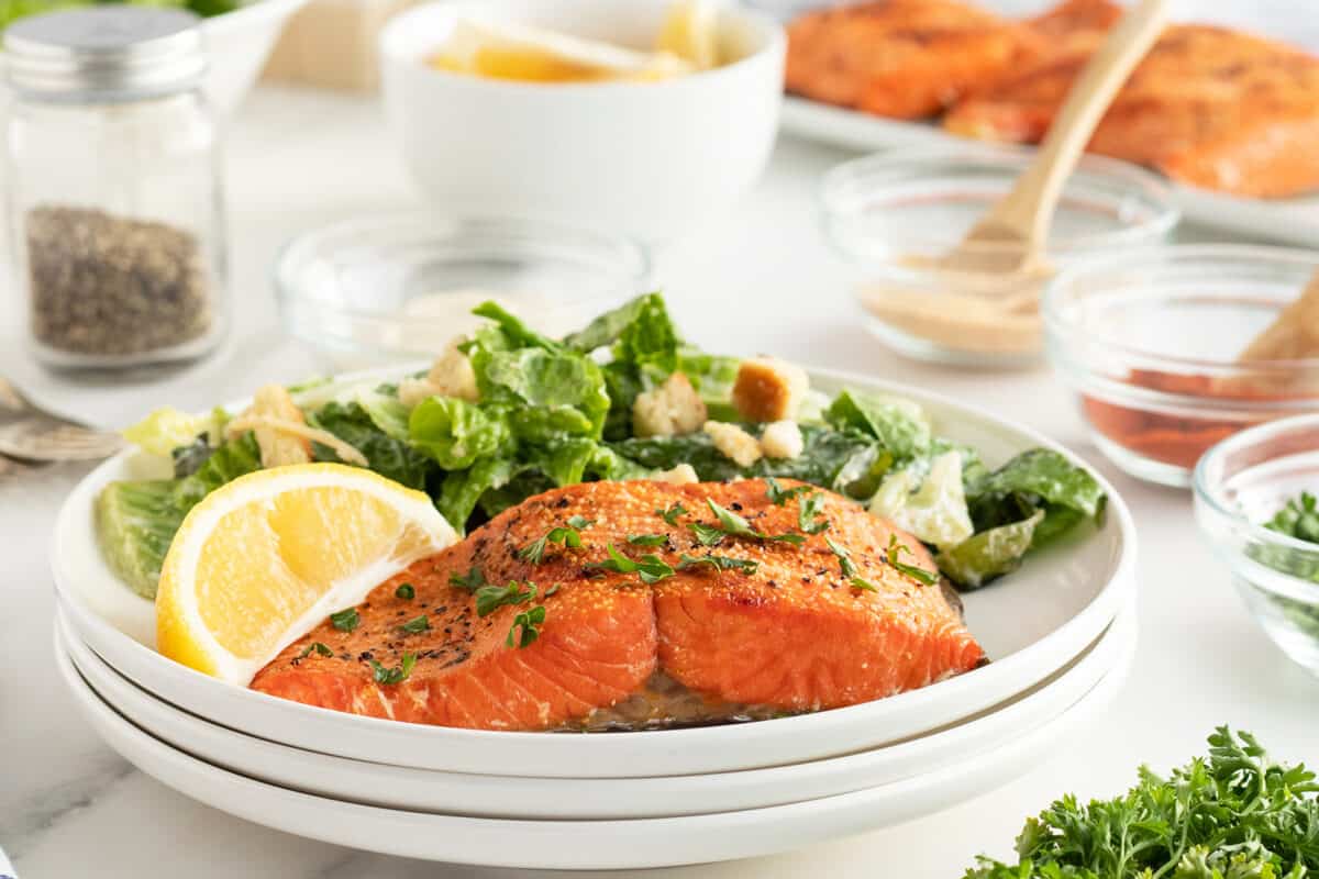 Air fryer salmon on a stack of white plates with a salad beside