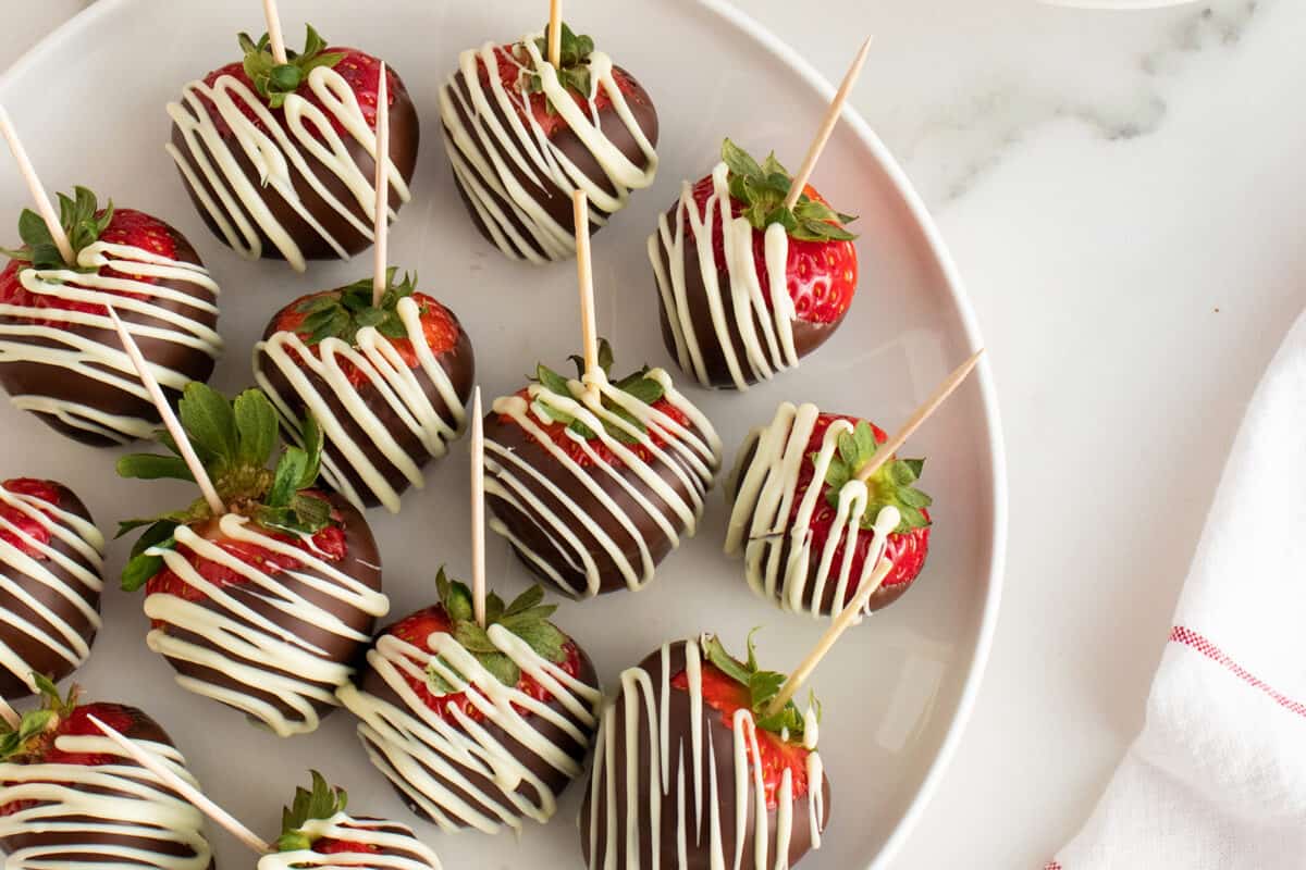 Chocolate covered strawberries on a white plate with toothpicks in them