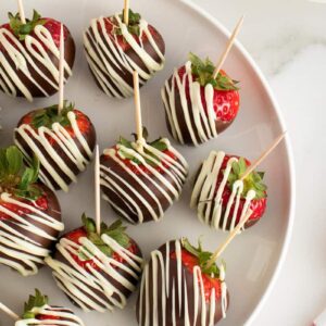 Chocolate covered strawberries on a white plate with toothpicks in them