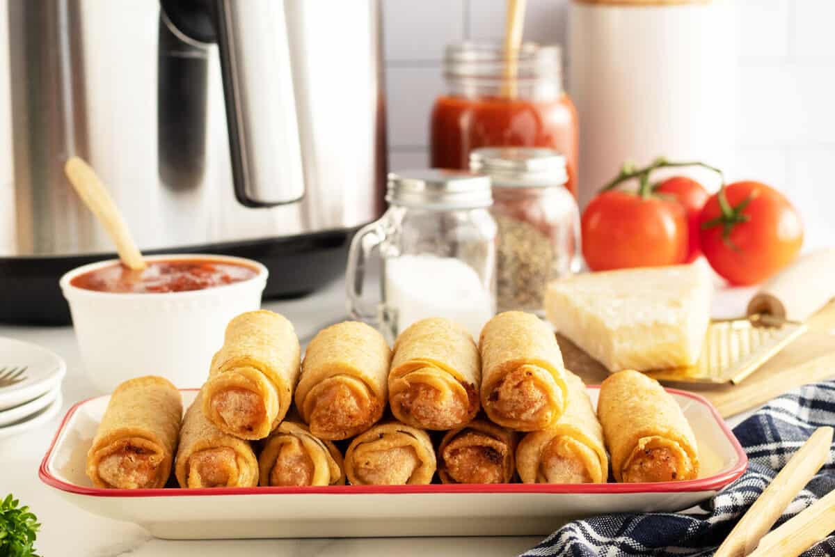 air fryer pizza rolls on a long platter with ingredients behind it like marinara sauce and salt and pepper