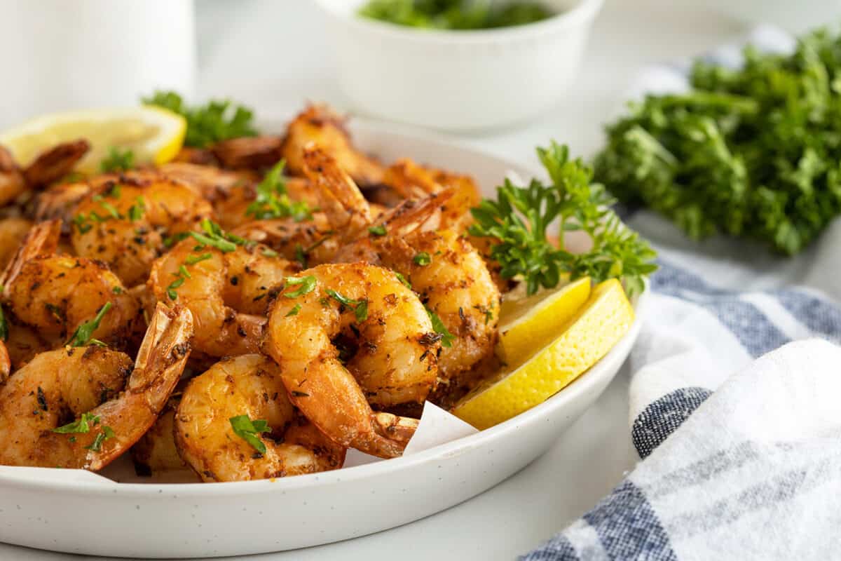 Air fryer shrimp stacked on a white plate with chopped parsley on top