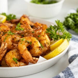Air fryer shrimp stacked on a white plate with chopped parsley on top