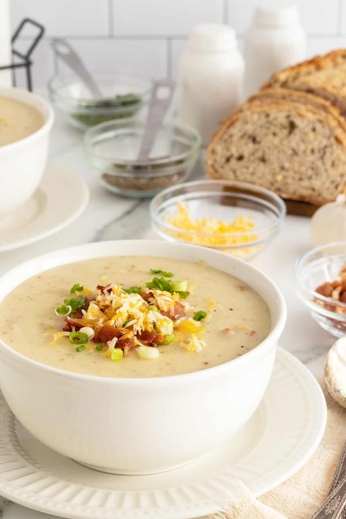 cream of potato soup with toppings and a loaf of rye bread behind it