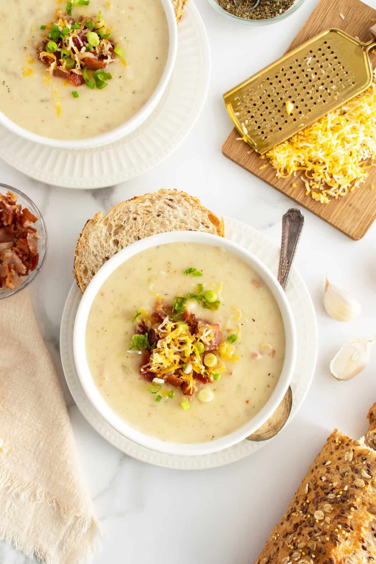 cream of potato soup in two white bowls with toppipngs nad cheese grated on a cutting board