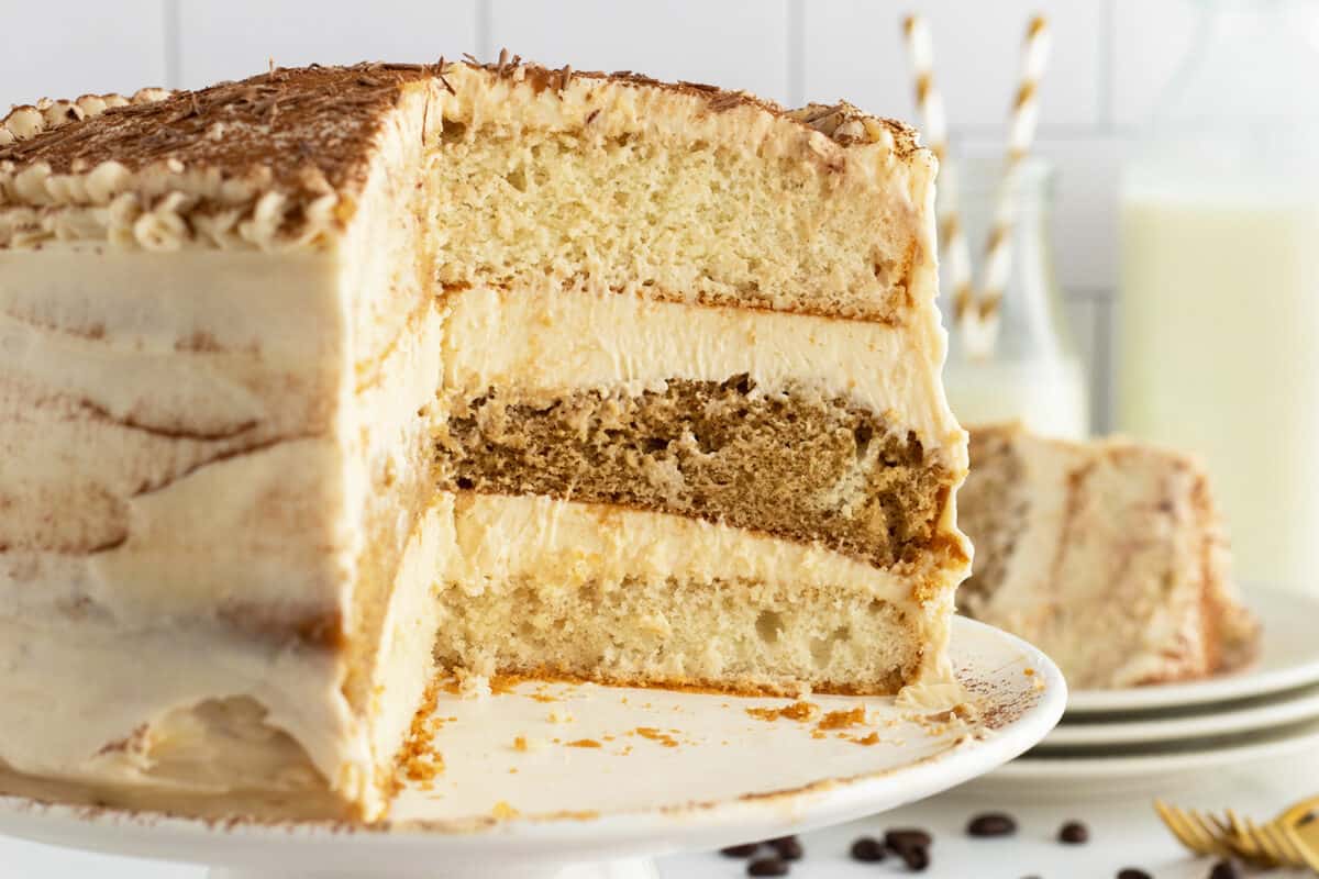 tiramisu cake on a white pedestal with a slice cut out