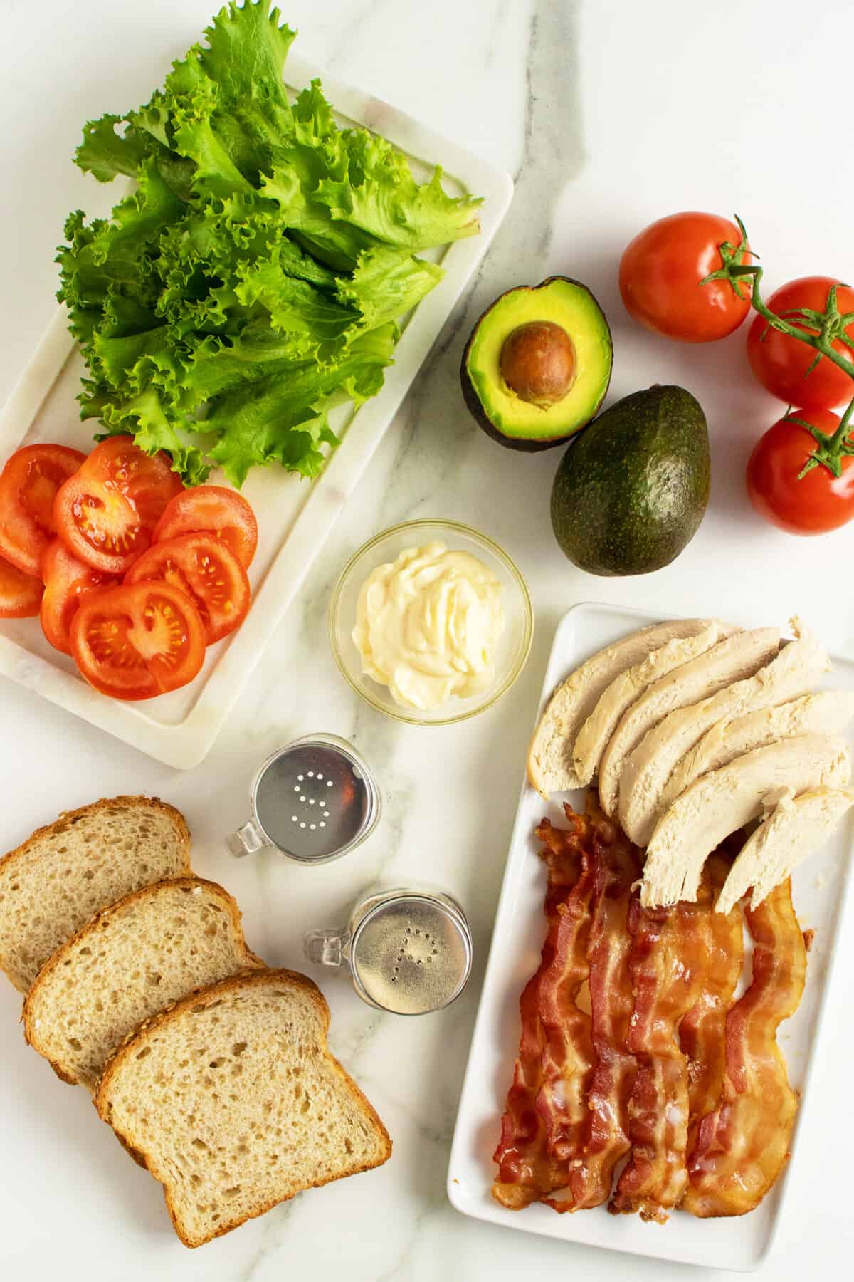 Turkey club sandwich ingredients laid out on two white platters with ingredients inbetween