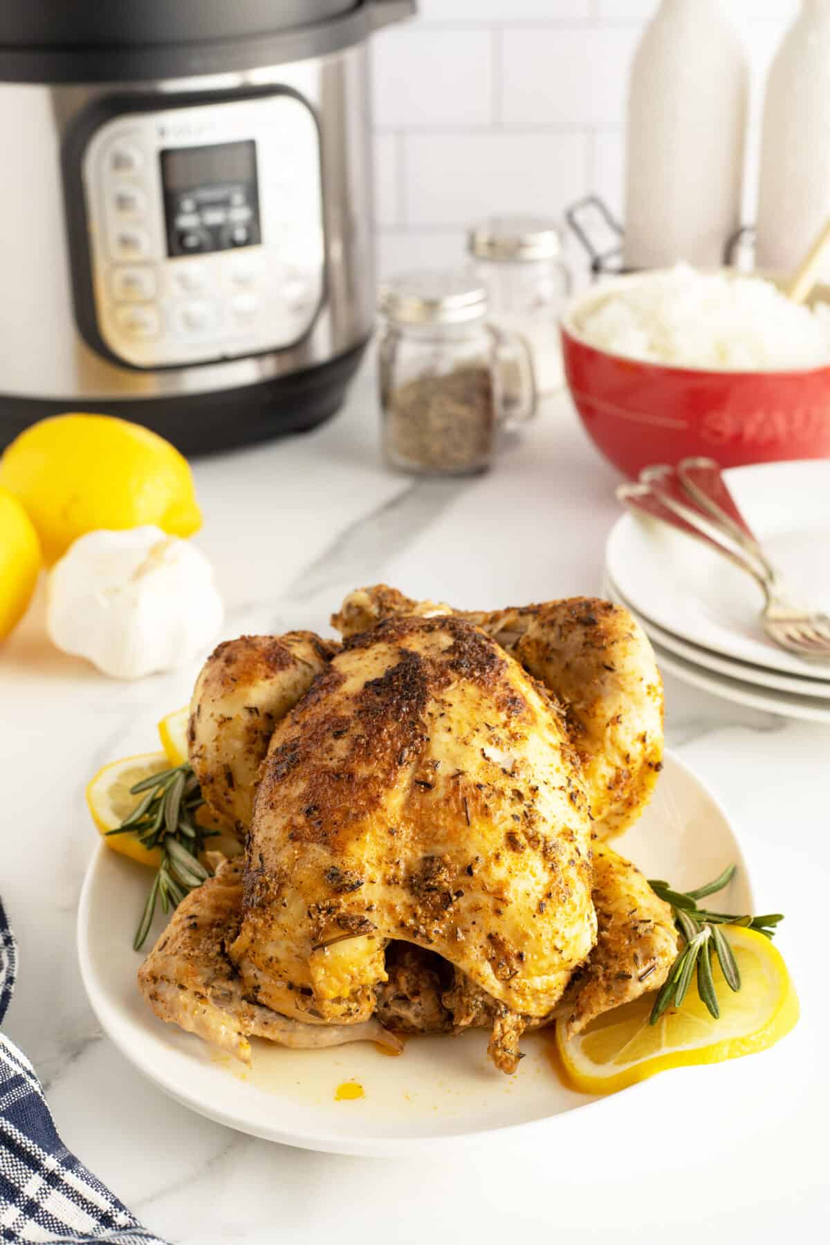 Instant Pot Whole Chicken on a white platter with lemon and rosemary sprigs around it