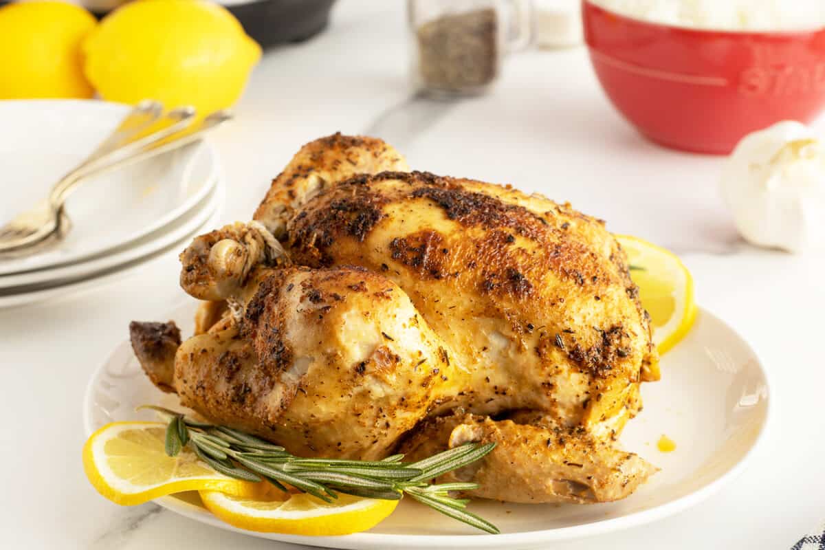 Instant Pot Whole Chicken on a white platter with rosemary and sliced lemon