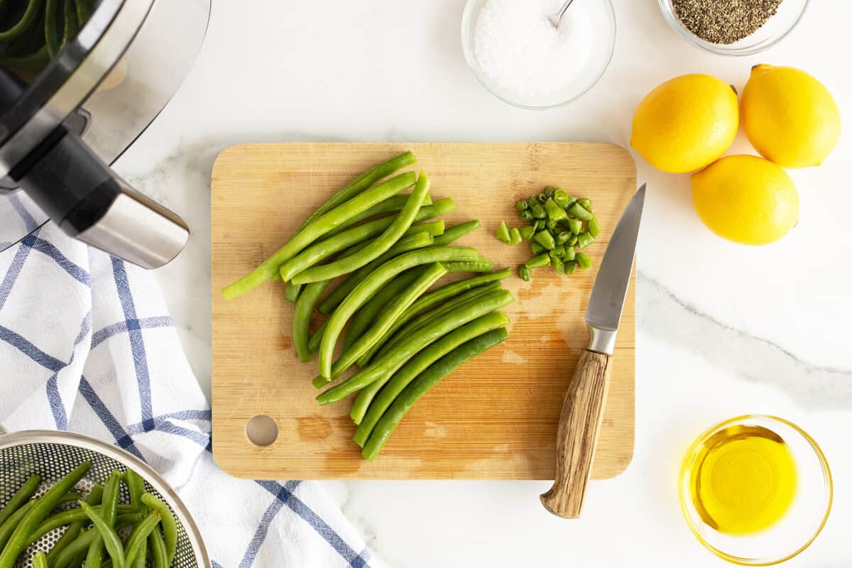 trimmed green beans on a wooden cutting board with a knife at the side