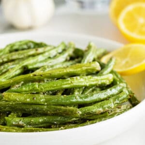 airfryer green beans on a white platter with slives of lemon