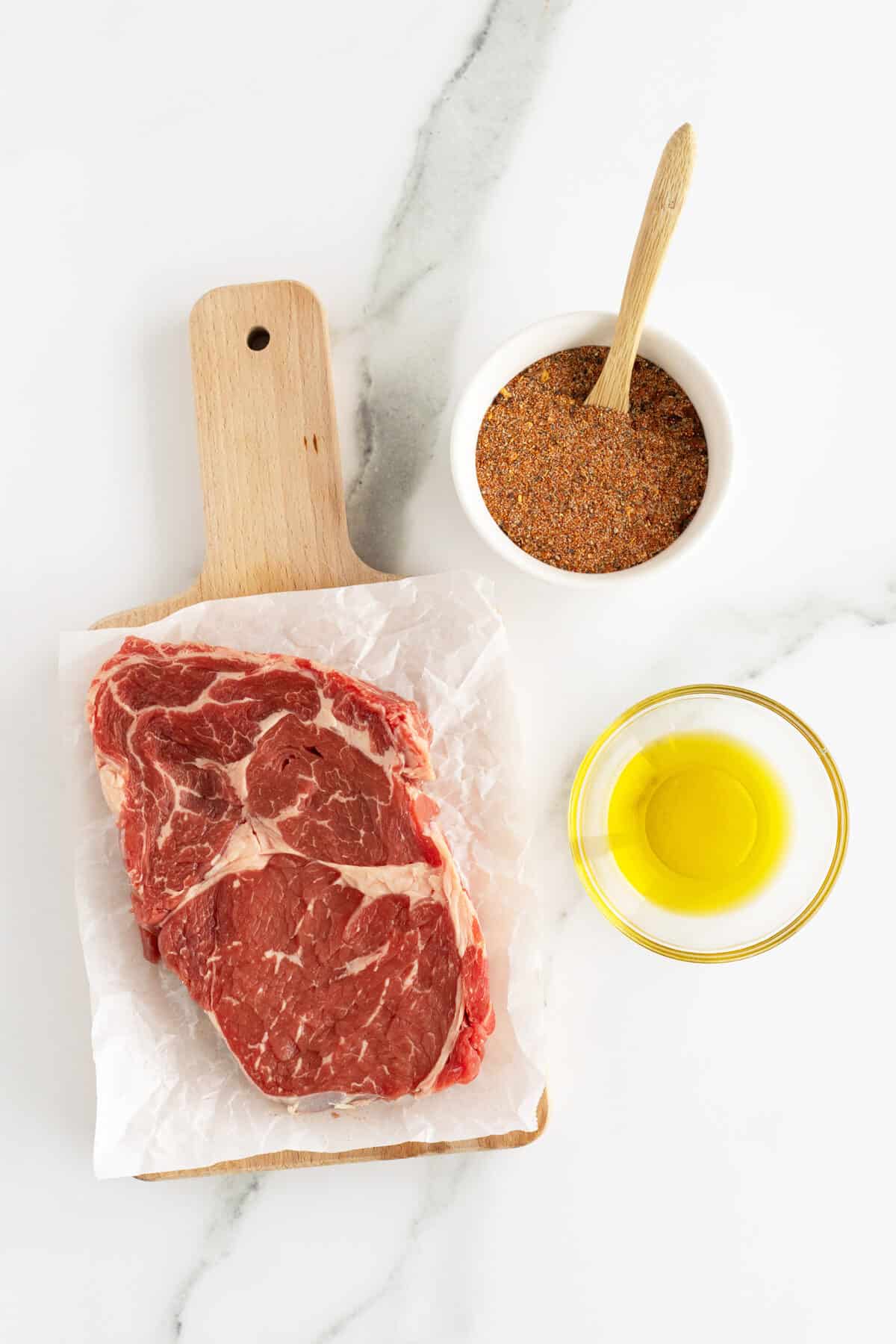 air fryer steak ingredients  in small bowls and the steak on parchment paper