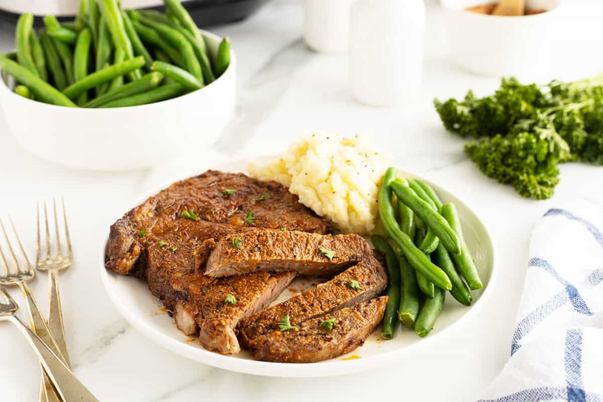 air fryer steak sliced ona white plate with green brans