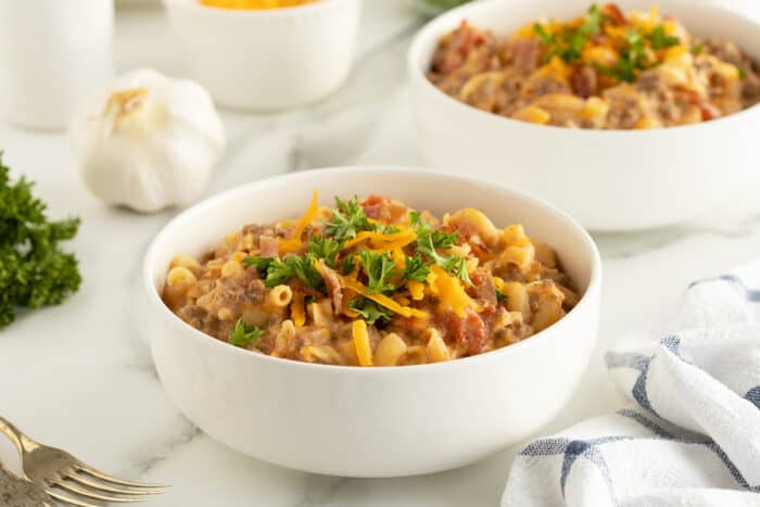 cheeseburger casserole in a large white bowl with cheese and garnish on top