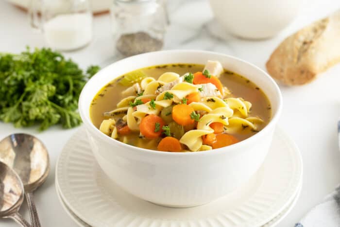 chicken noodle soup in a large white bowl with spoons beside