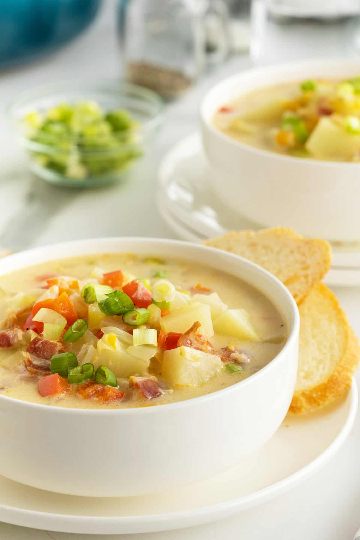 corn chowder in a white bowl with slices of baguette beside it