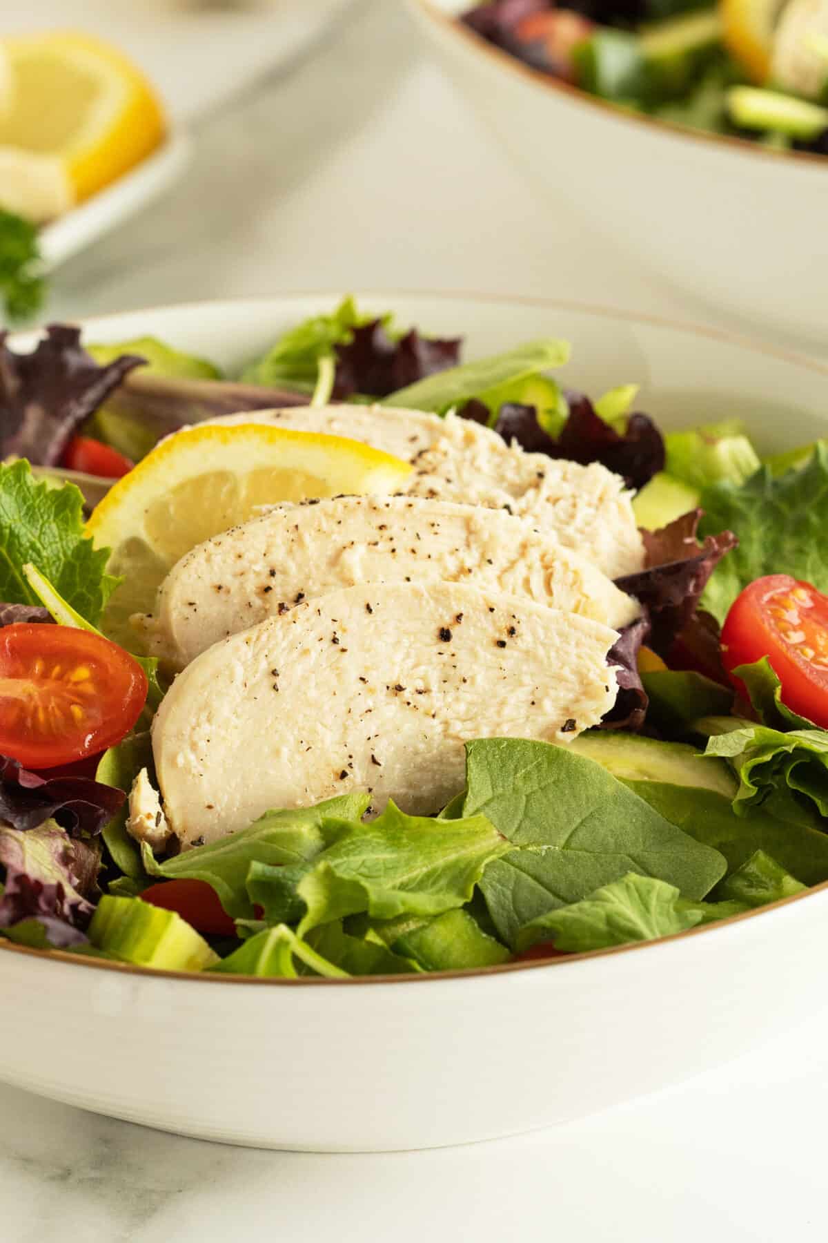 poached chicken in a bowl on top of lettuce and cherry tomatoes