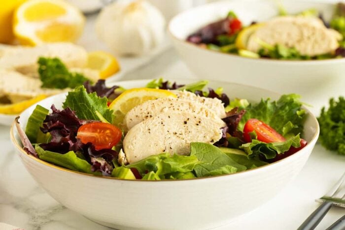 poached chicken in a bowl on a bed of lettuce and tomatoes