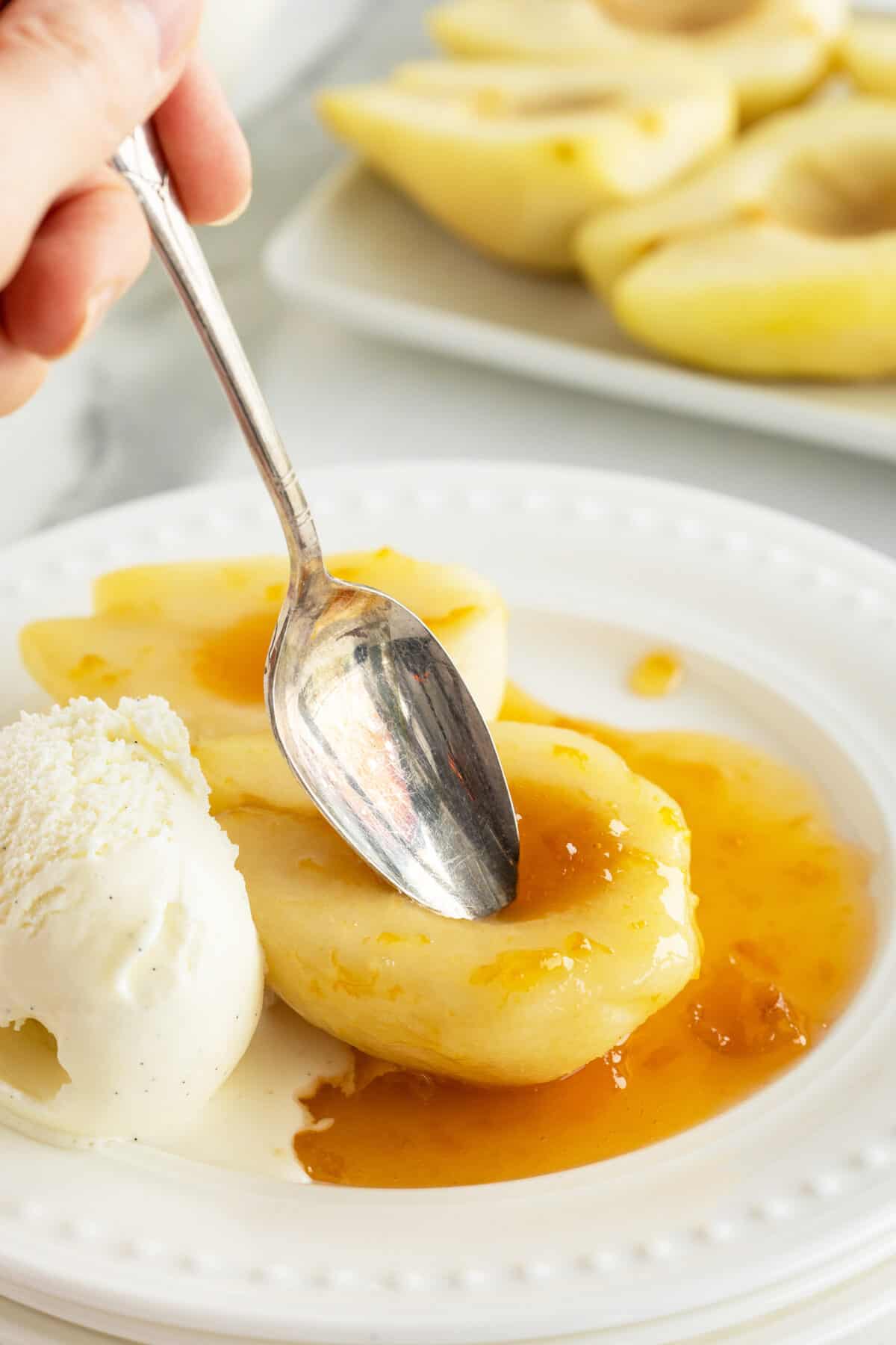 Poached pears on a white plate with a spoon in one pear