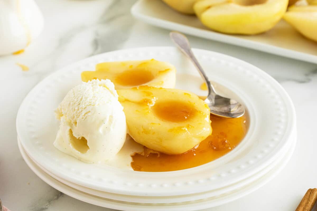 Poached pears on a white sauce with a scoop of vanilla ice cream melting on the plate