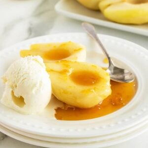 Poached pears on a white sauce with a scoop of vanilla ice cream melting on the plate