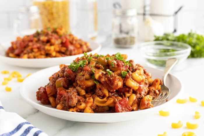 American chop suey on a white plate with a fork on the side