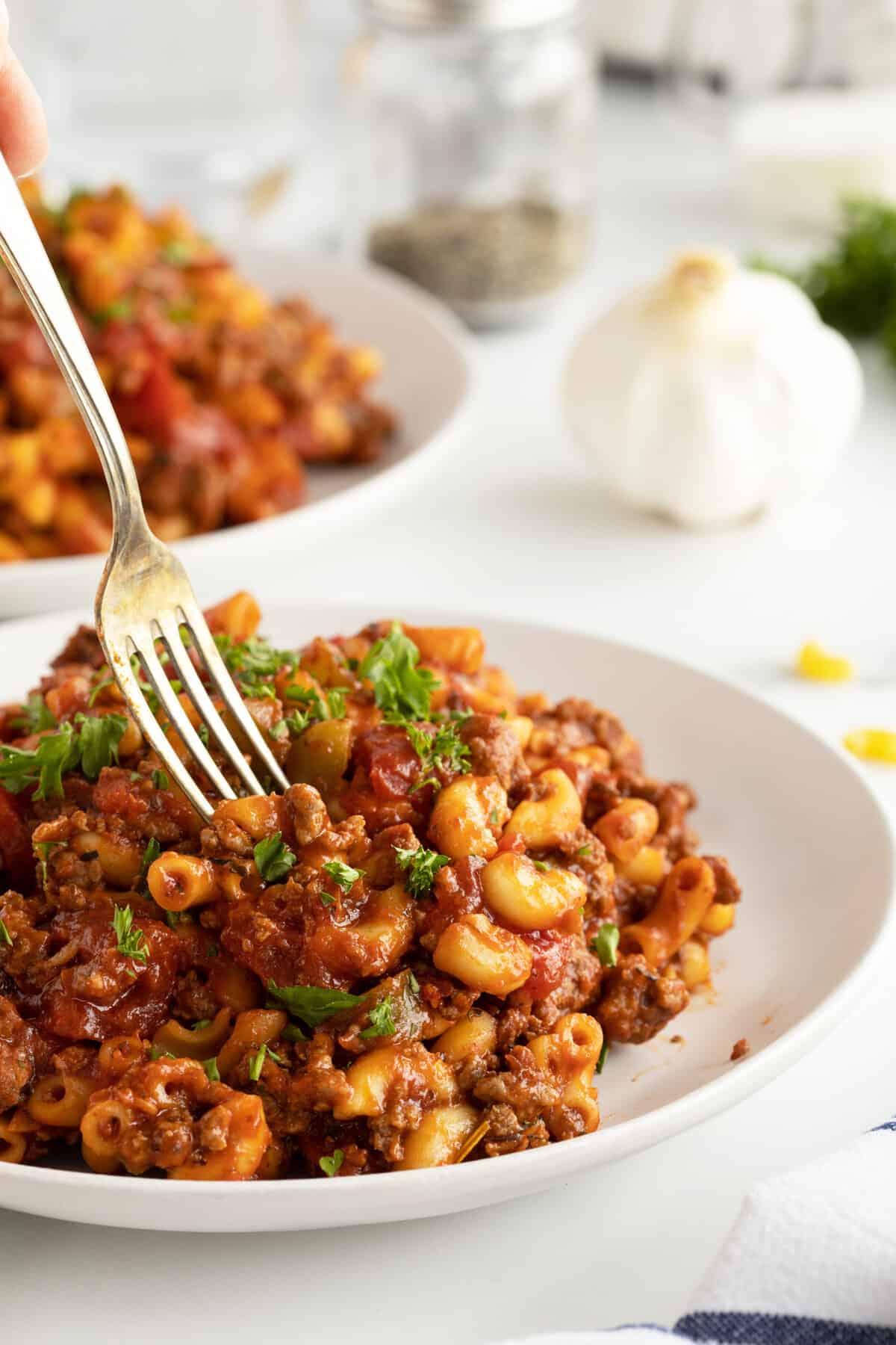 American chop suey on a white plate with a fork digging into the center of the dish