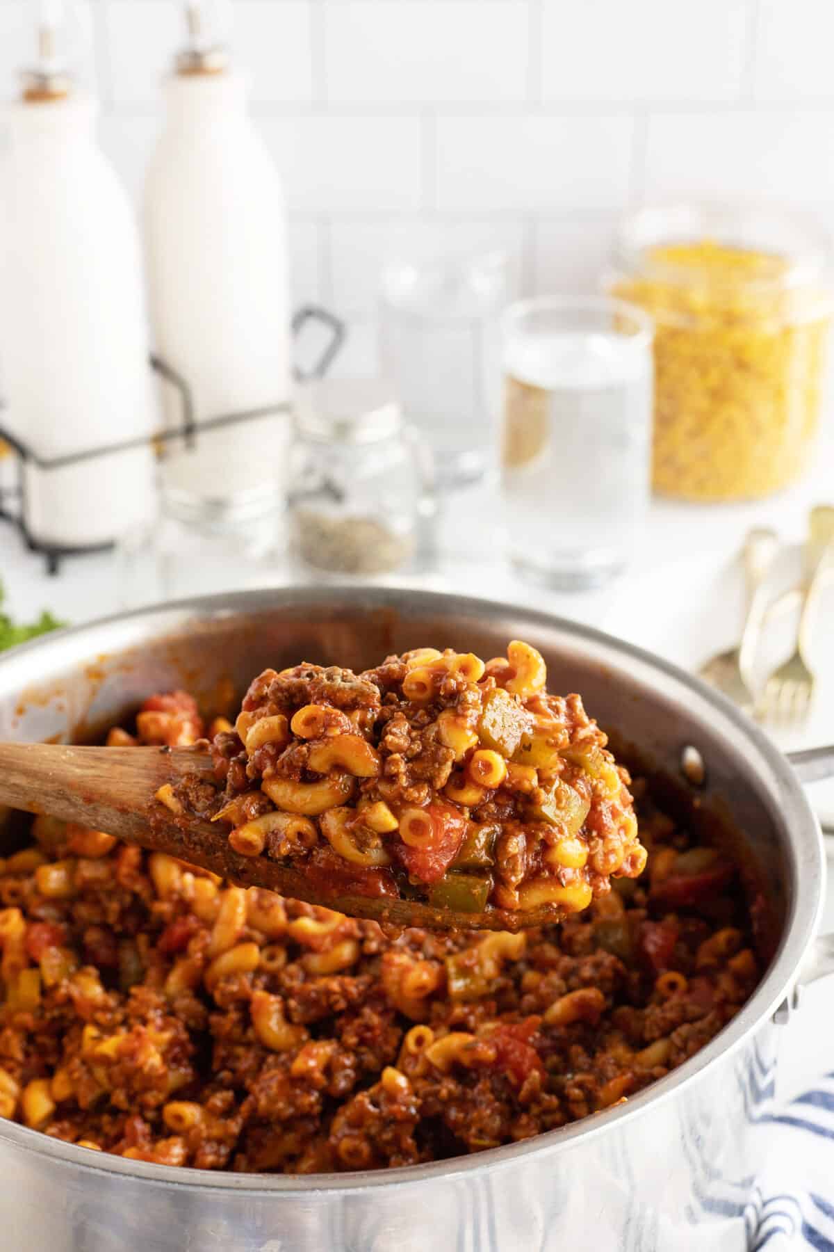 American chop suey in a pot and a large wooden spoon full being held over the pot