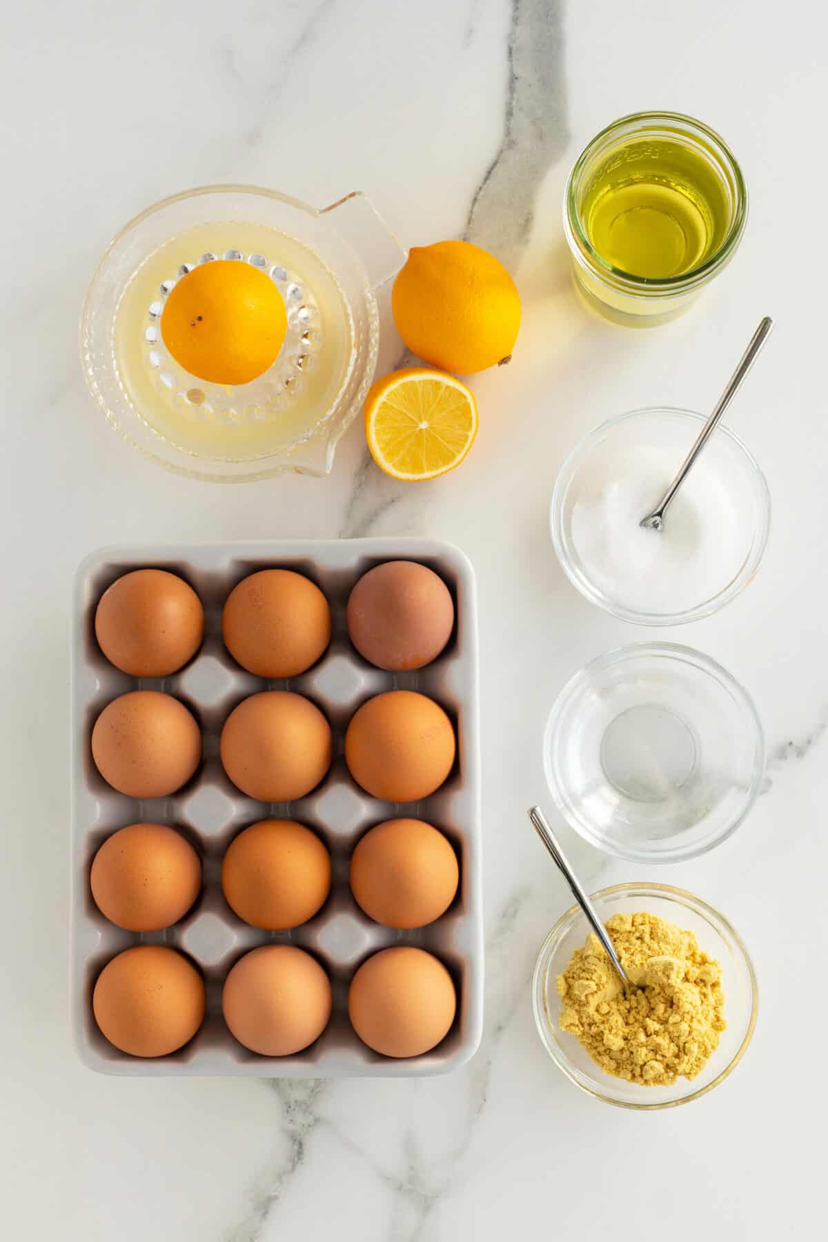 homemade mayonnaise ingredients in small clear bowls with a carton of eggs